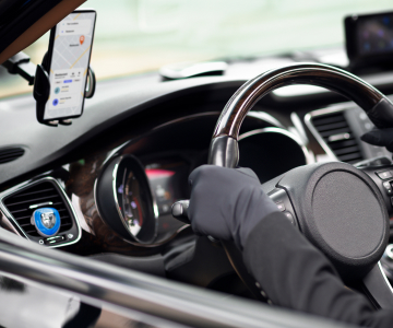 car interior and gloved hands on the steering wheel, smartphone with a map above the steering wheel
